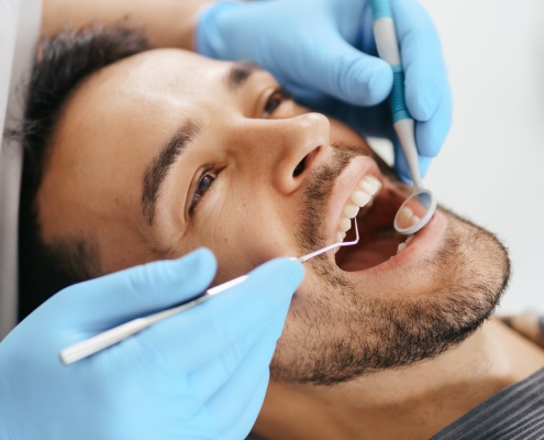 smiling-young-man-sitting-dentist-chair-while-doctor-examining-his-teeth