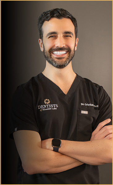 Portrait of Dr. Cristian Löfvall, a friendly and professional dentist at Dentists of Hinsdale Lake, dressed in a black clinic uniform with his name and title embroidered, smiling confidently with arms crossed.