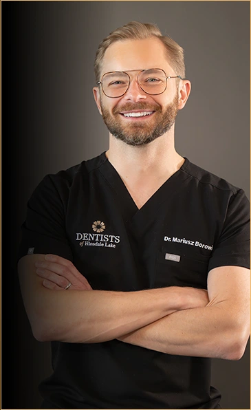 Portrait of Dr. Mariusz Borowicz, an experienced dentist with a friendly demeanor, dressed in a black Dentists of Hinsdale Lake uniform, arms crossed, and smiling, signifying professionalism and a welcoming approach to dental care.