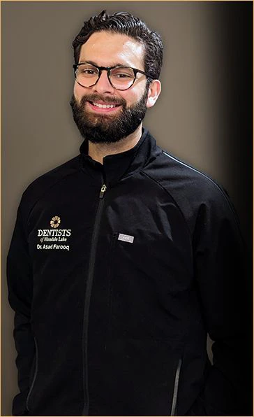 Professional portrait of Dr. Asad Farooq, a member of the American Academy of Cosmetic Dentistry, sporting a friendly smile in his Dentists of Hinsdale Lake jacket, exemplifying his dedication to personalized and innovative dental care.